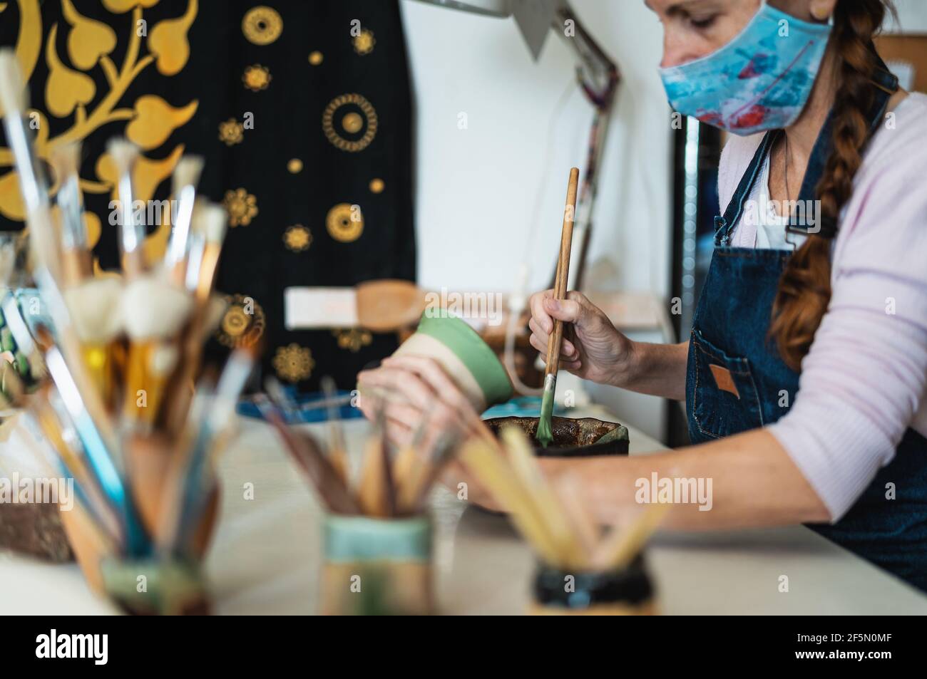 Woman potter painting clay pot in workshop during corona virus outbreak - Artisan work and creative craft concept Stock Photo
