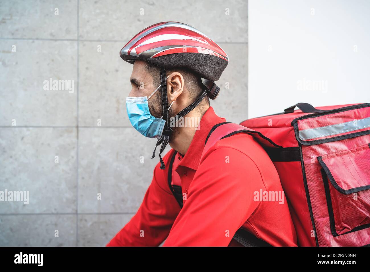Rider man delivering meal to customers with electric bicycle while wearing face mask during corona virus outbreak - Eco fast delivery food concept Stock Photo