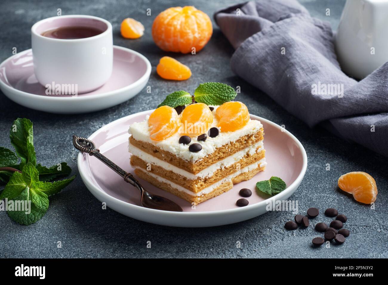 Sponge cake layers with buttercream, decorated with slices of tangerine chocolate and mint. Delicious sweet dessert for tea Stock Photo