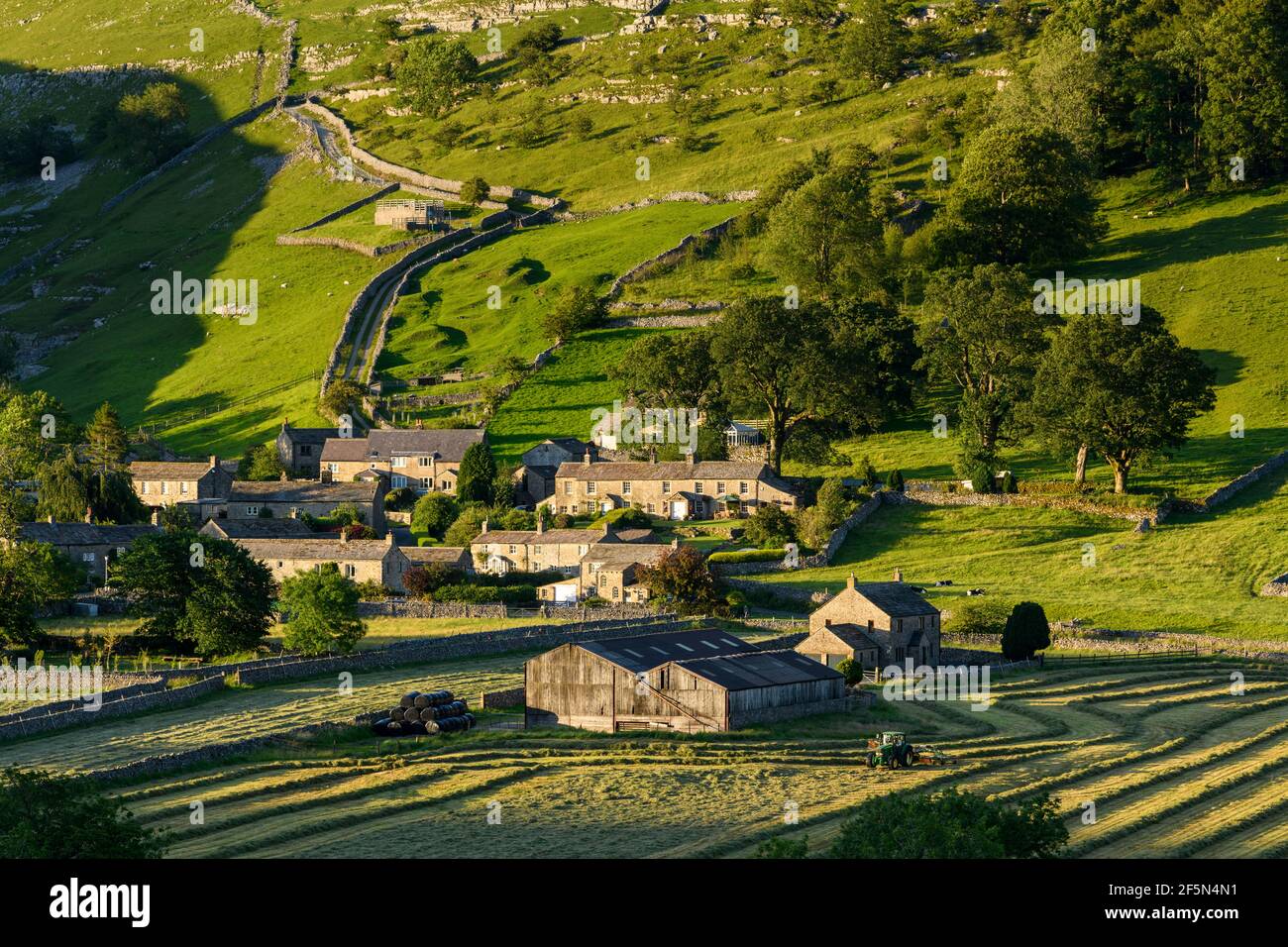 Picturesque Dales valley & tiny village, houses, barn, farmland fields, hill, steep hillside & tractor hay-making - Starbotton, Yorkshire, England UK. Stock Photo