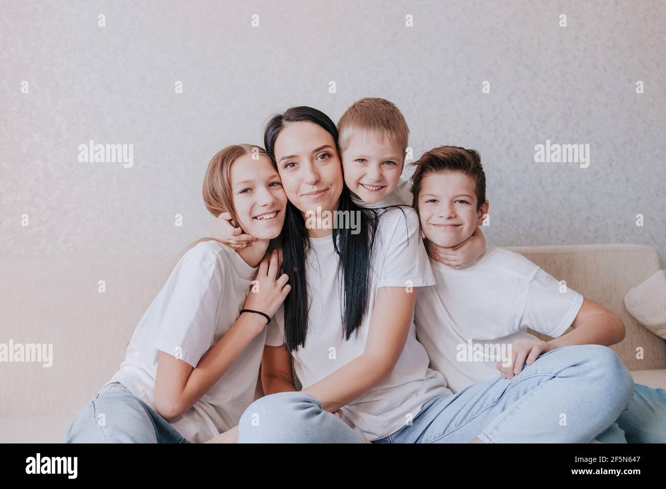 A happy mom sits at home on the couch in the arms of her children. Understanding supporting the trust of an idyllic concept Stock Photo