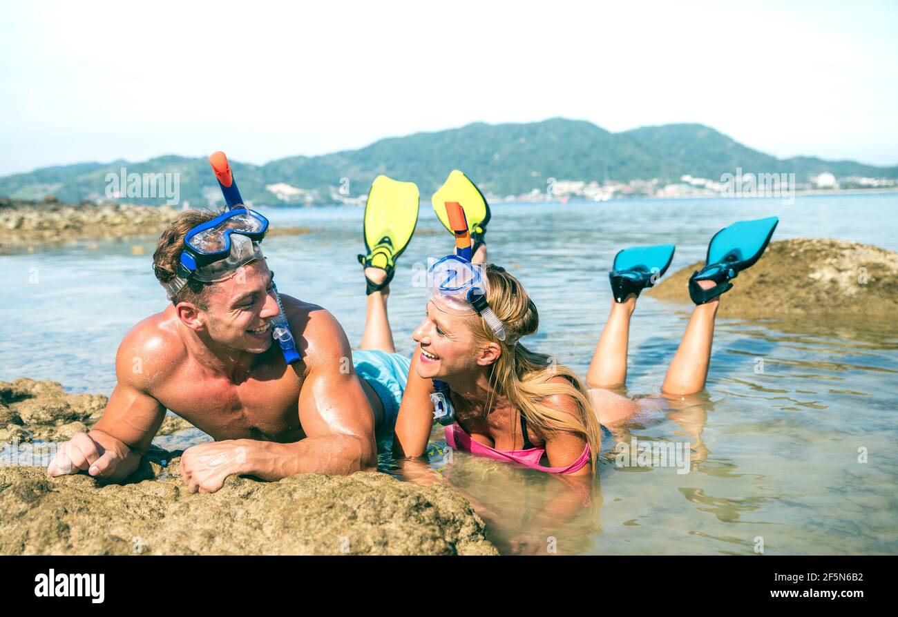 Happy couple of vacationer in love having fun at water on tropical beach in Thailand with snorkel mask and fins - Active youth travel concept Stock Photo