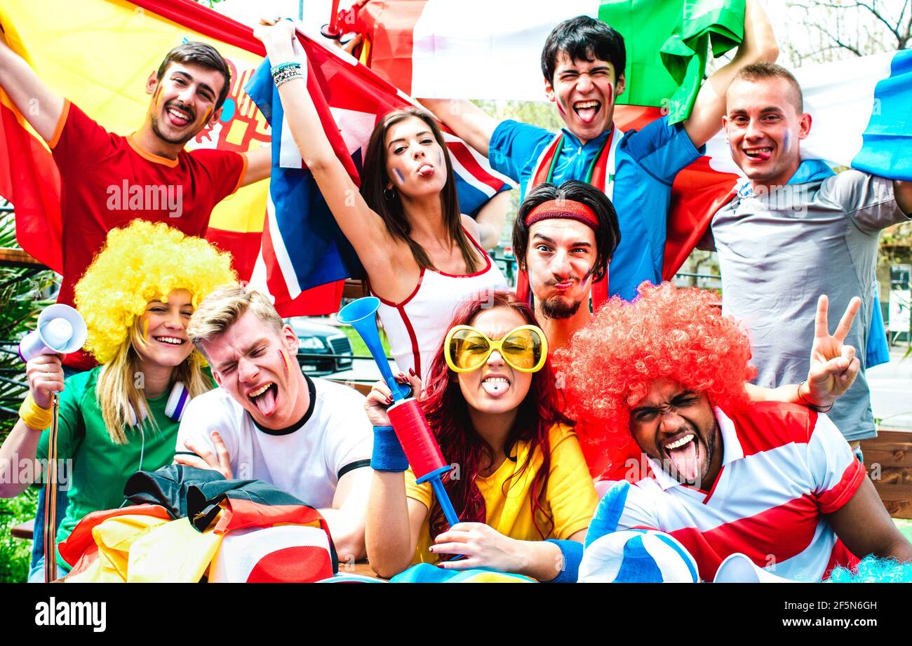 Young football supporter fans cheering with international flags at soccer match - Happy people with multicolored tshirts having fun together outdoors Stock Photo