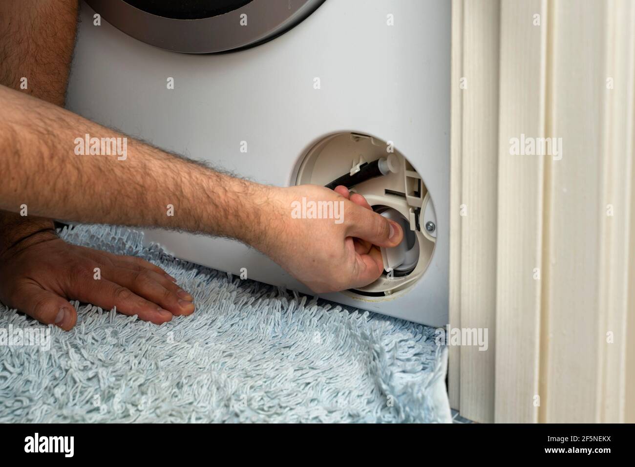 the master opens the filter of the washing machine to remove the blockage. Problem with Laundry. Stock Photo