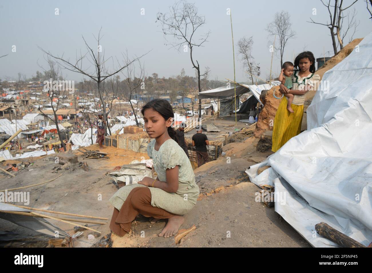 A girl seating beside her temporary shelters set up for displaced Rohingya refugees days after a fire at a refugee camp in Ukhia, in the southeastern Stock Photo