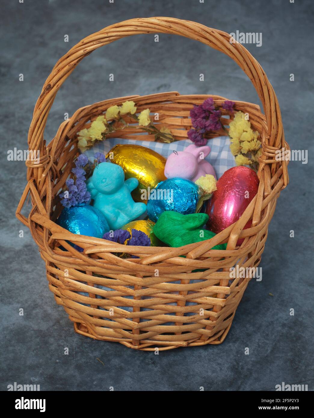 Basket with easter eggs in colored tin foil, bunnies and flowers. Stock Photo