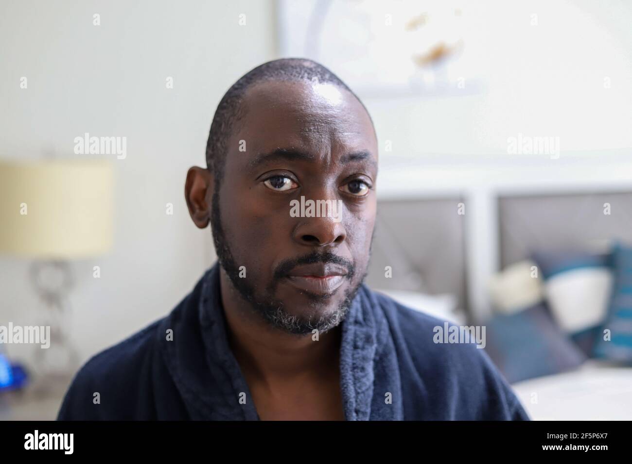 A portrait of a African-American man sitting on a bed and looking sad and depressed Stock Photo
