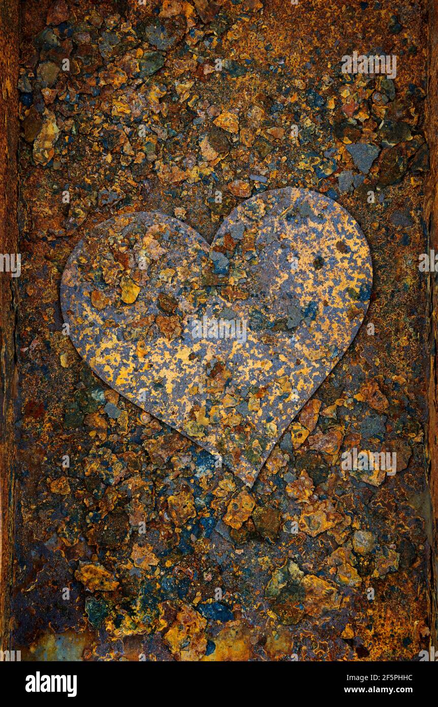 Rusty metal heart on corroded and rusting steel ash pan. After years of use and exposure to heat and solid fuel ash the pan was left out in th erain f Stock Photo