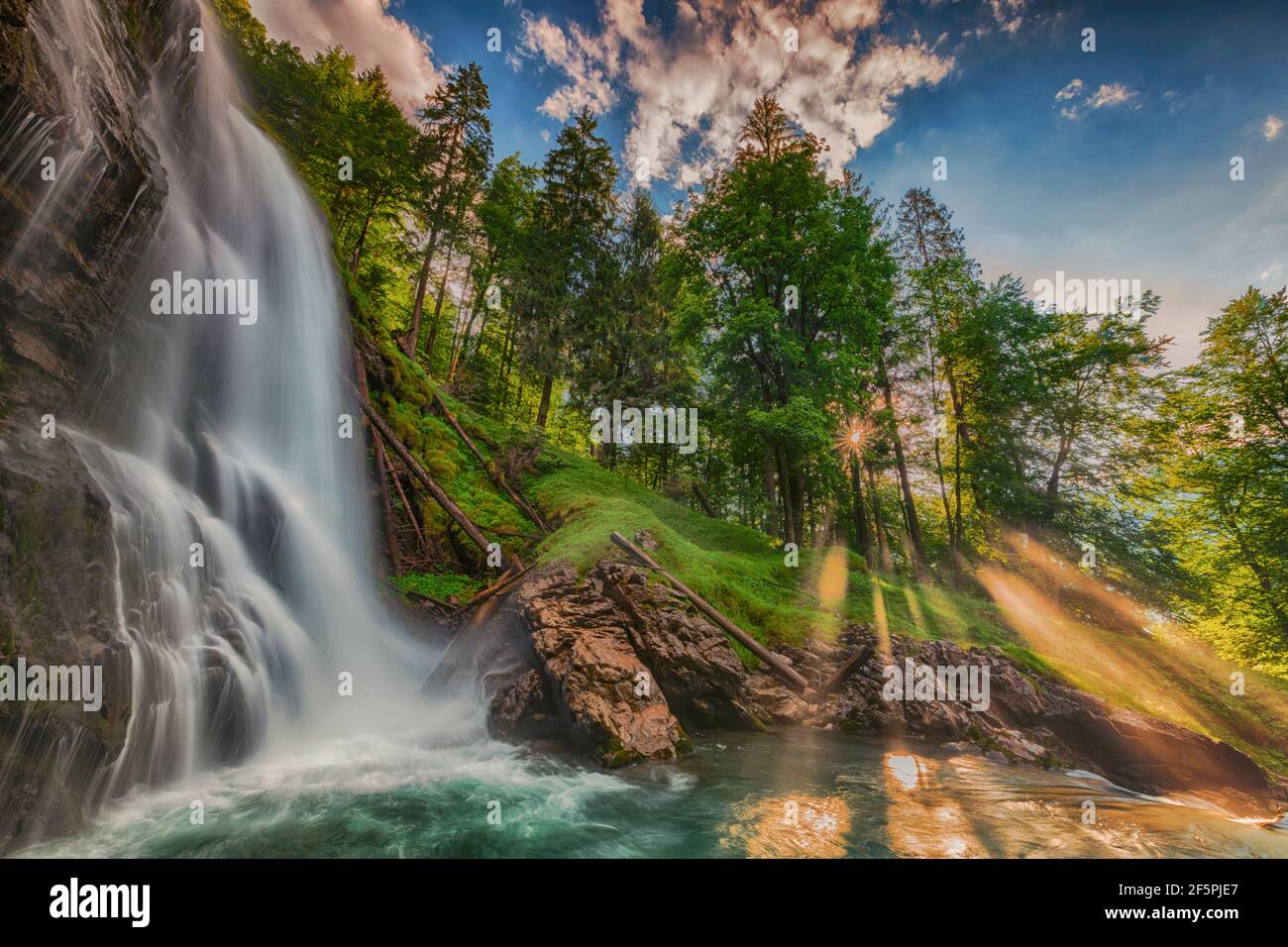 Gorgeous view of a waterfall in the forest with the sun shining through ...