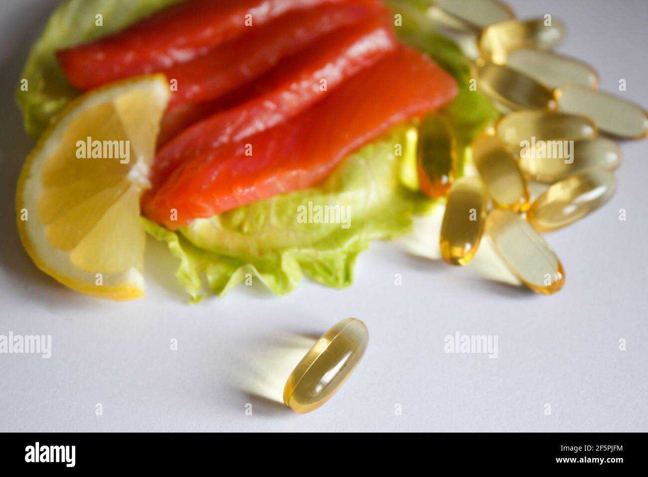 Omega-3 fish oil capsules pills and salmon fillet slice with lemon and lettuce leaf. Stock Photo