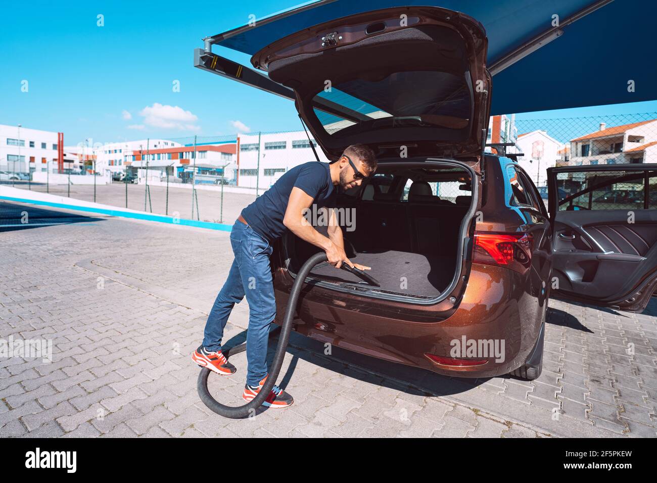 Young attractive man cleaning car inside with vacuum cleaner at self