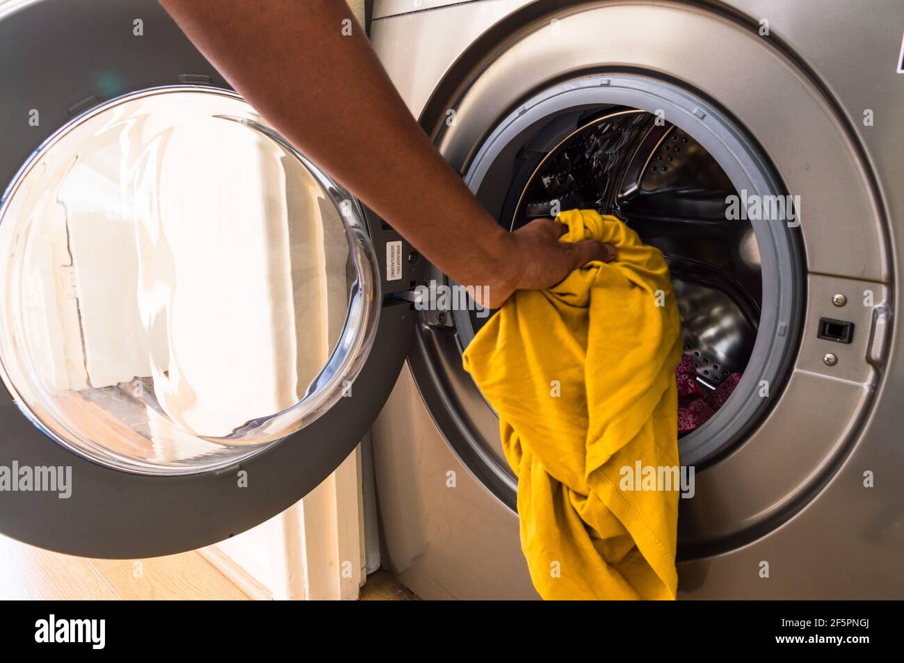 Adult middle aged Asian man loading washing machine with soiled clothes Stock Photo