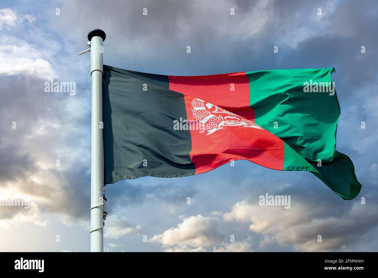 Afghanistan sign symbol. Afghani national flag on a pole waving against cloudy sky background. Stock Photo