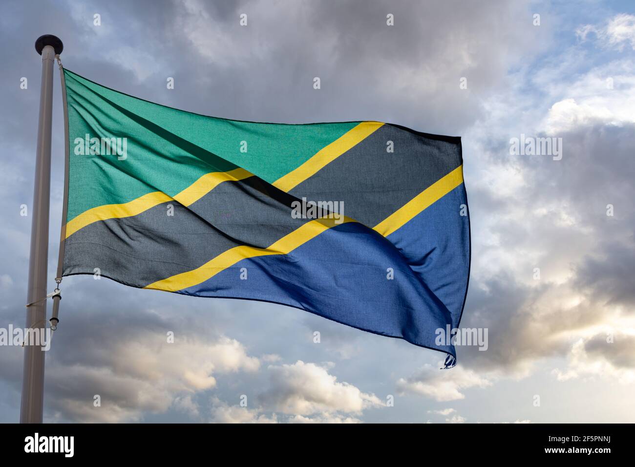 Tanzania sign symbol. United Republic of Tanzania national flag on a pole waving against cloudy sky background. Stock Photo