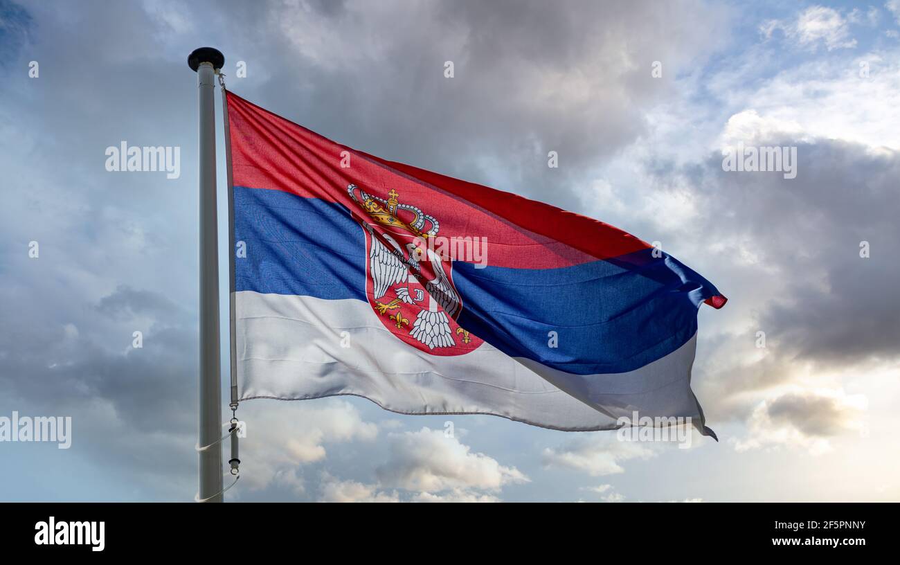 Serbia sign symbol. Serbian national flag on a pole waving against cloudy sky background. Stock Photo