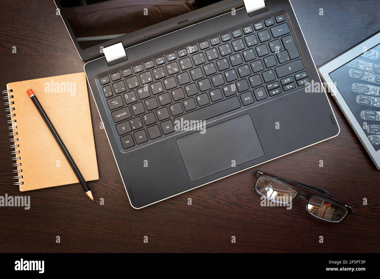 Working place with laptop, e-book reader, notepad, pencil and glasses on dark wood background. Business and education concept. Stock Photo