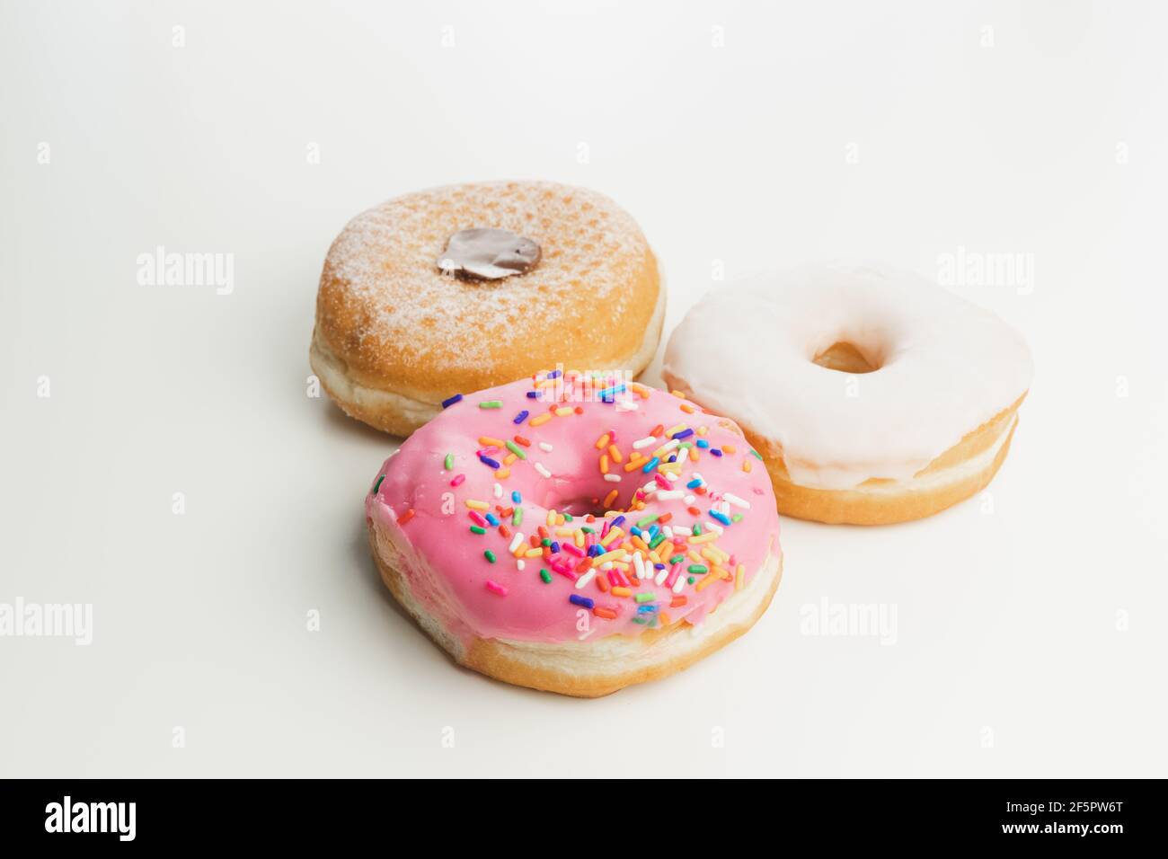 Three fresh, colourful ring doughnuts isolated on a plain white surface and background. Stock Photo