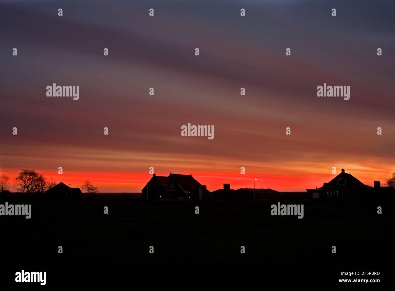 Fiery sky over silhouettes of farmhouses before sunrise on the Dutch island Terschelling Stock Photo