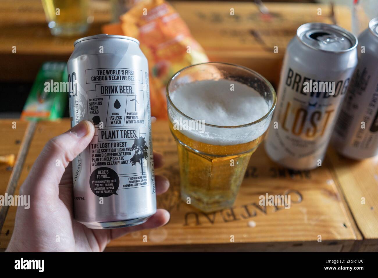 A man's hand holding a can and a glass of Brew Dog Lost Lager, a pilsner brewed using wind power & is the world's first carbon negative beer Stock Photo