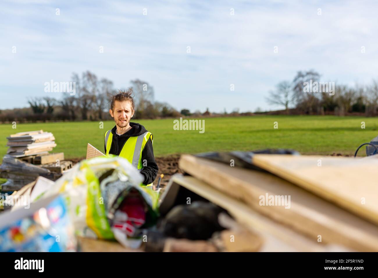 A young adult male builder wearing a high visibility vest throwing rubbish into a skip Stock Photo