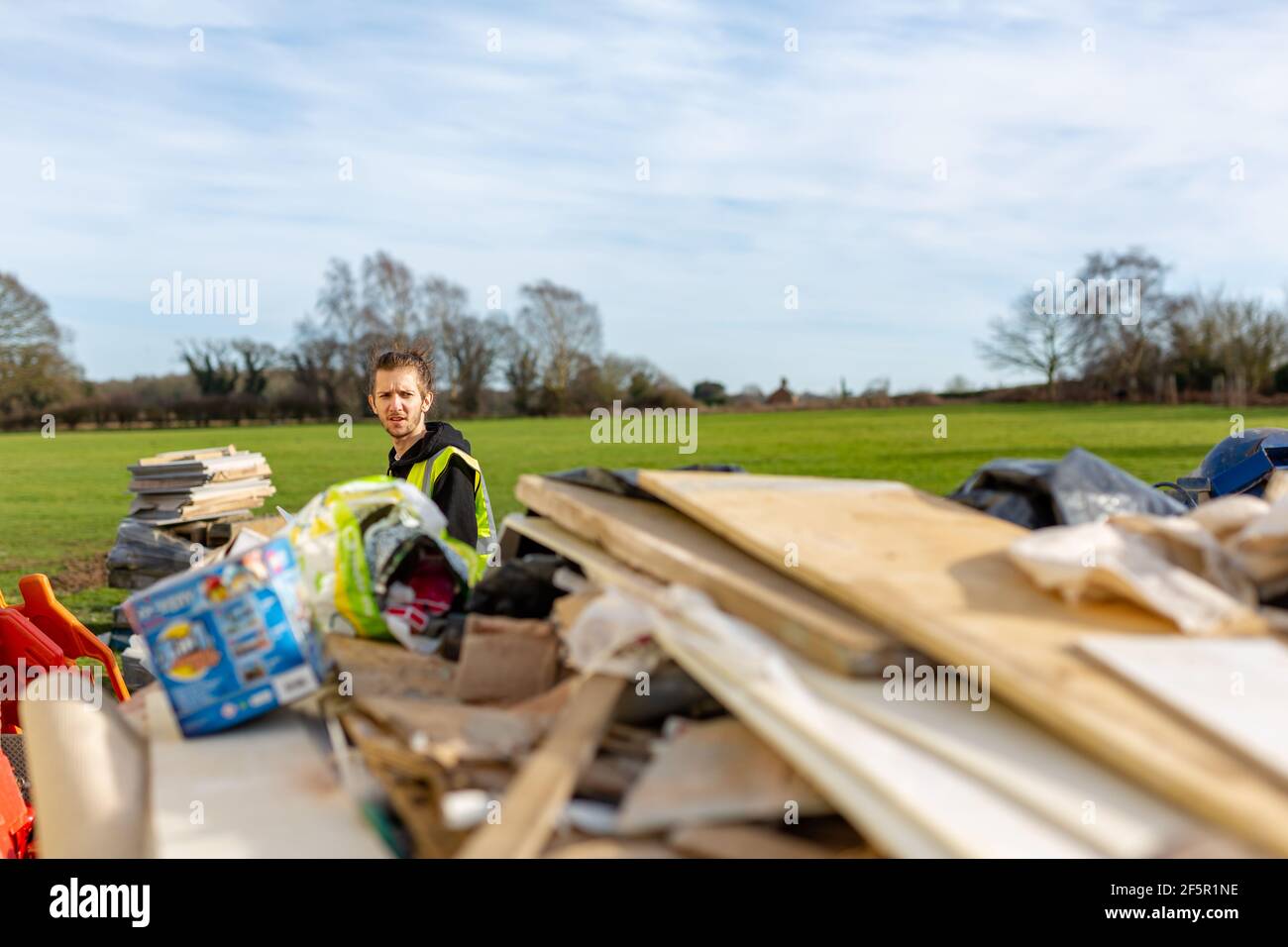 A young adult male builder wearing a high visibility vest throwing rubbish into a skip Stock Photo