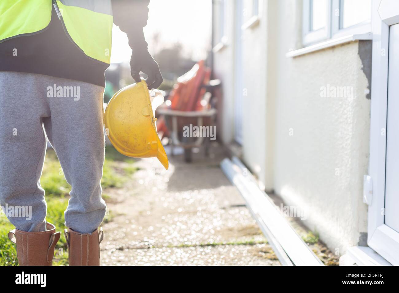 A close-up of an unknown builder wearing a high visibility vest and holding a hard hat. Builder, safety, building site, laborer concept Stock Photo
