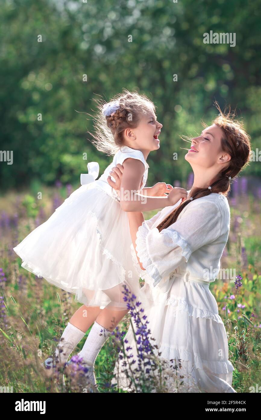 Happy family activities and outdoors lifestyle on a summer meadow with grass and flowers. Little girl child daughter playing and kissing mother huggin Stock Photo
