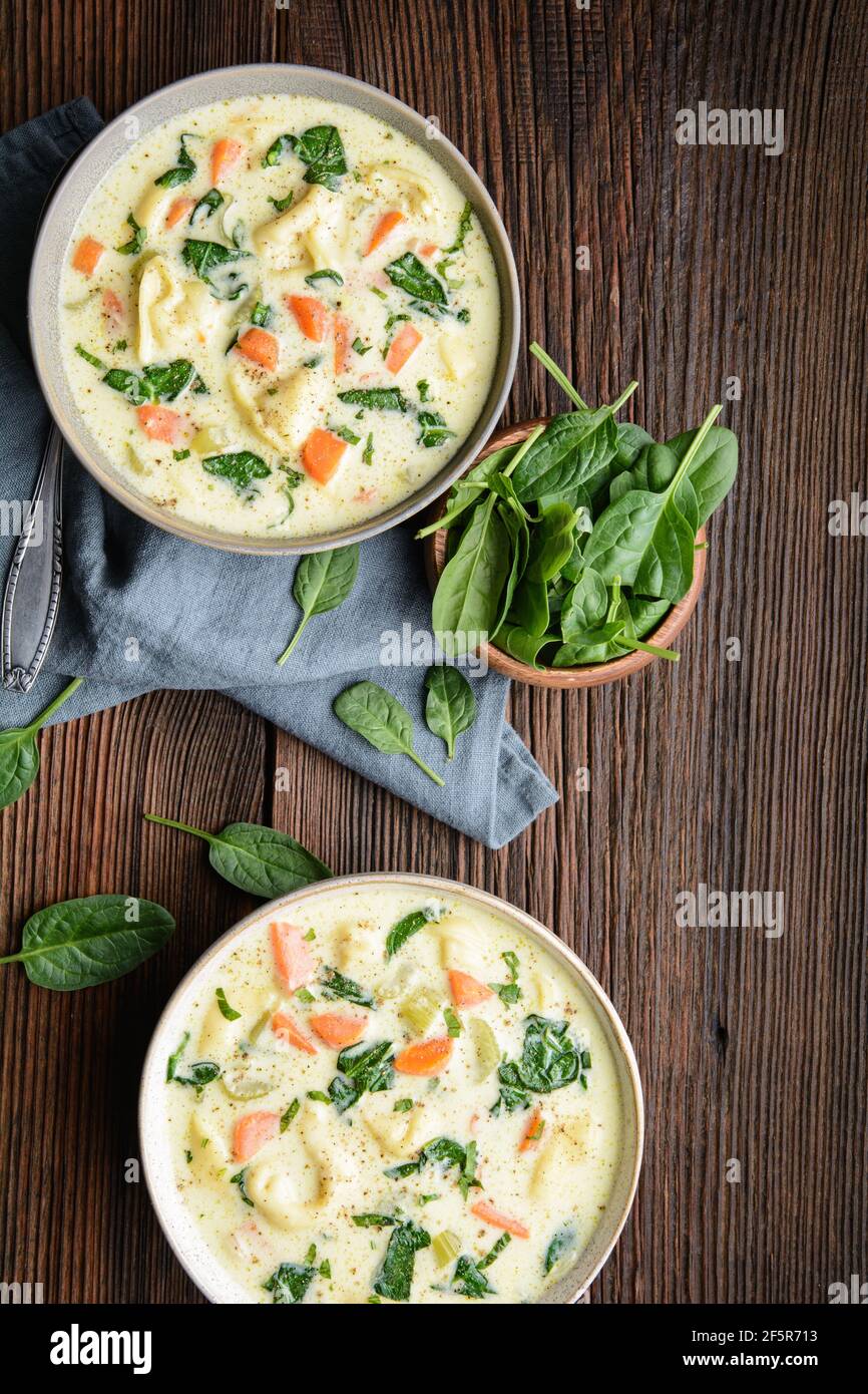 Comforting creamy Tortellini pasta soup with spinach, celery, carrot and chicken broth on rustic wooden background Stock Photo