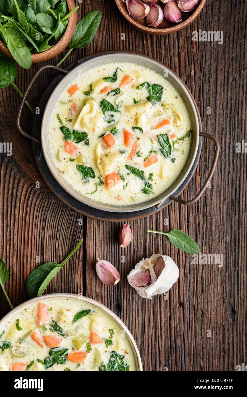Comforting creamy Tortellini pasta soup with spinach, celery, carrot and chicken broth on rustic wooden background Stock Photo