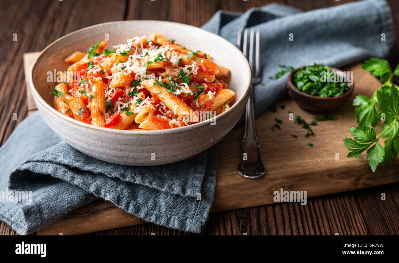 Classic penne all'Arabiata, spicy pasta with tomato and chilli sauce, topped with grated cheese on rustic wooden background Stock Photo