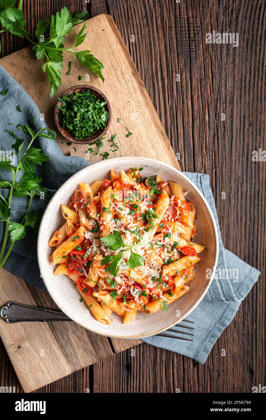 Classic penne all'Arabiata, spicy pasta with tomato and chilli sauce, topped with grated cheese on rustic wooden background Stock Photo