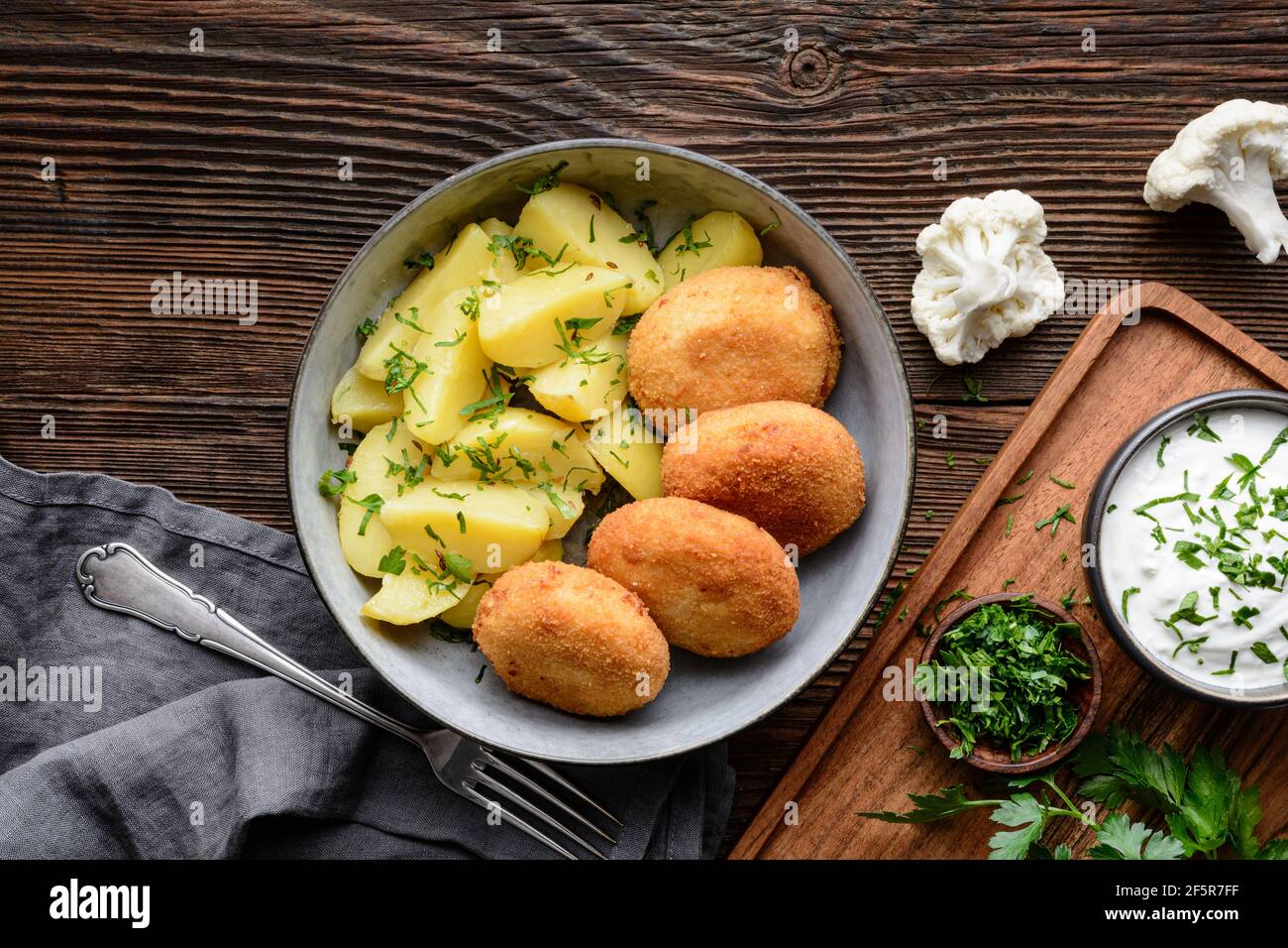 Fried cauliflower and cheese croquettes with boiled potatoes and sour cream dip on rustic wooden background Stock Photo