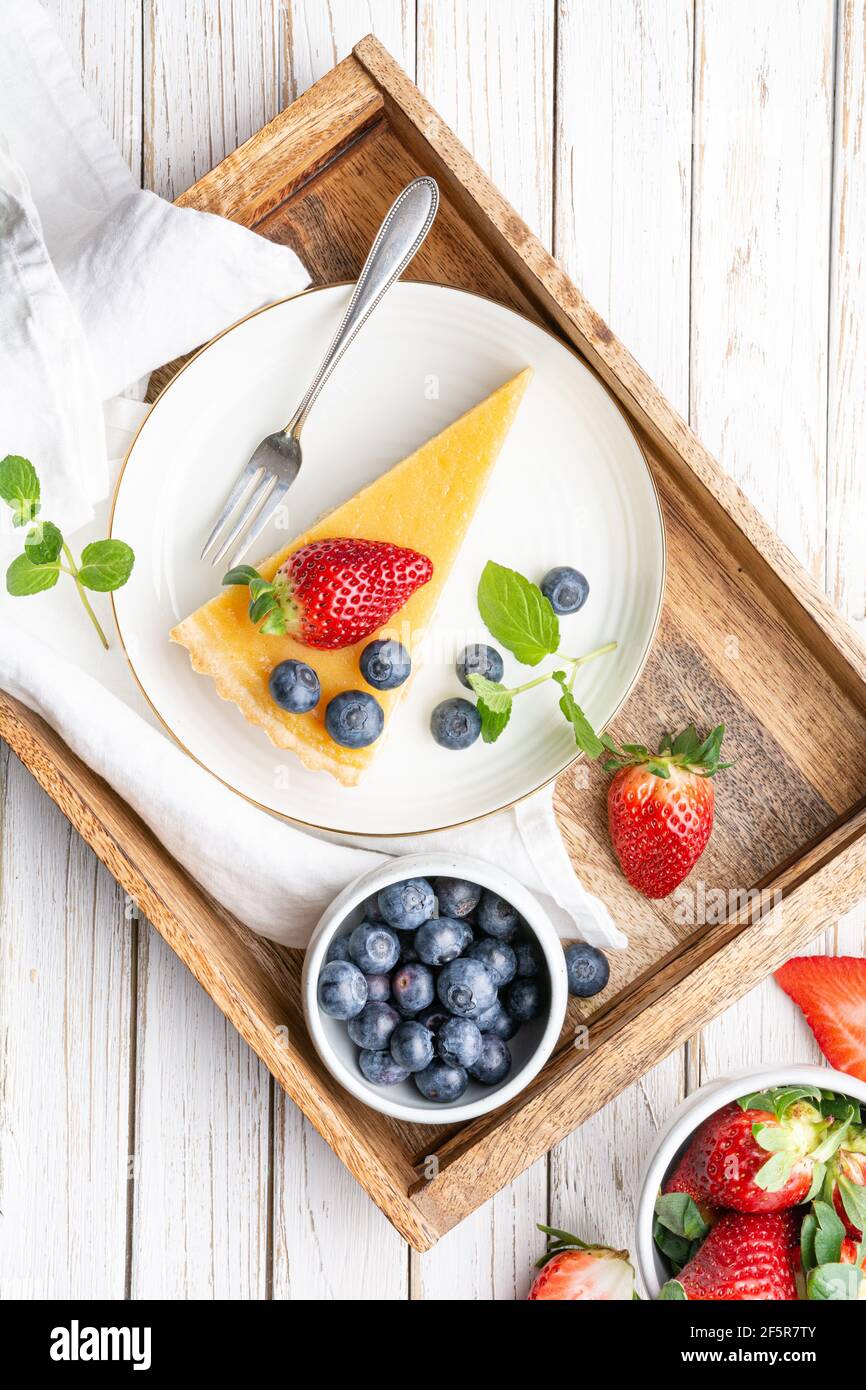 Cream cheese tart slices with lemon curd topping, served with fresh blueberries and strawberries on white rustic background Stock Photo
