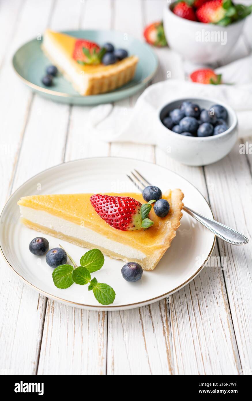 Cream cheese tart slices with lemon curd topping, served with fresh blueberries and strawberries on white rustic background Stock Photo