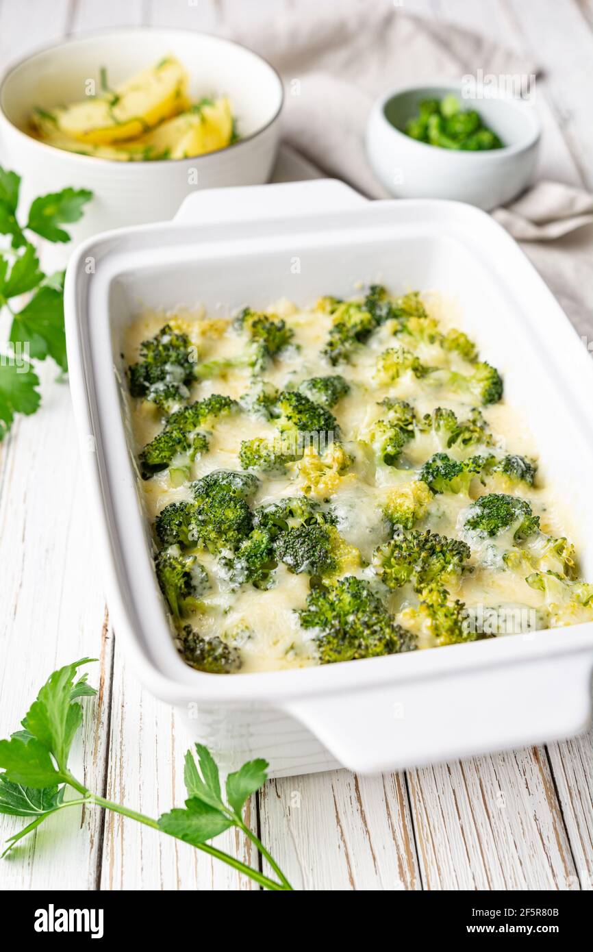 Simple broccoli and cheese casserole served with boiled potatoes on white wooden background Stock Photo