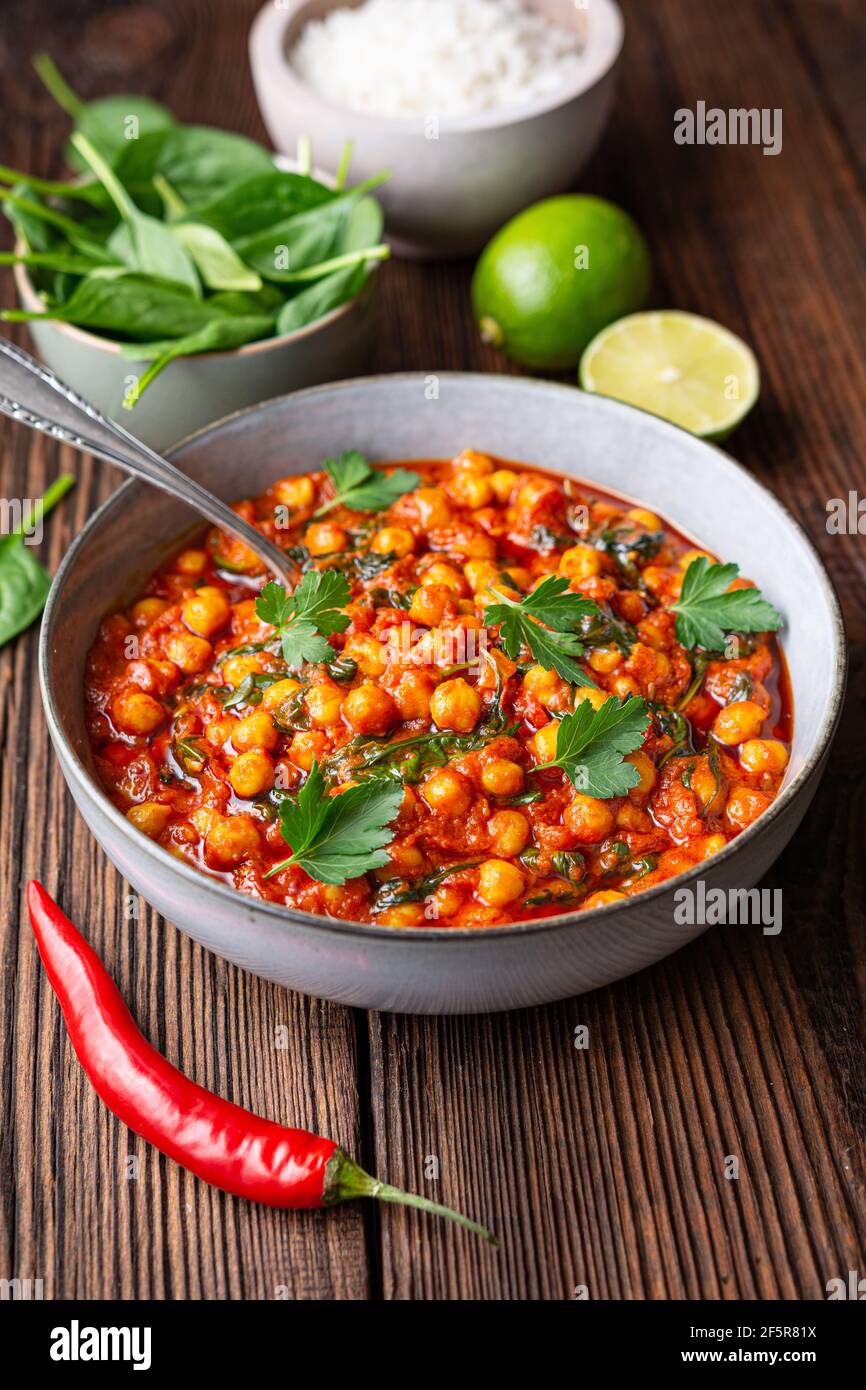 Indian meal, spicy chickpea curry with spinach in a bowl served with rice on rustic wooden background Stock Photo