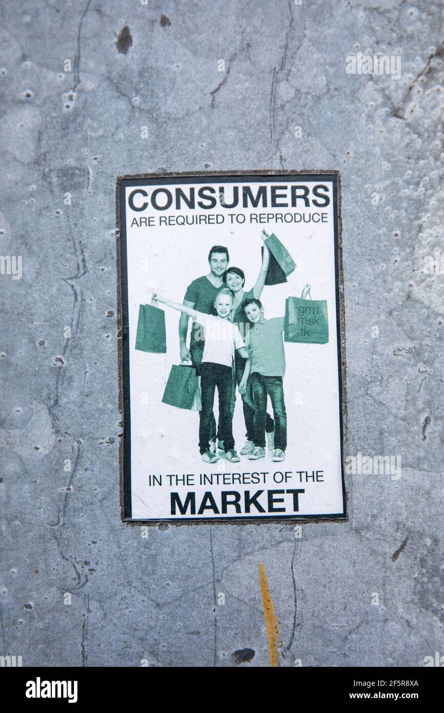 Consumers are required to reproduce in the interest of the market. Anti-consumerist sticker on an aluminum light pole. Stock Photo