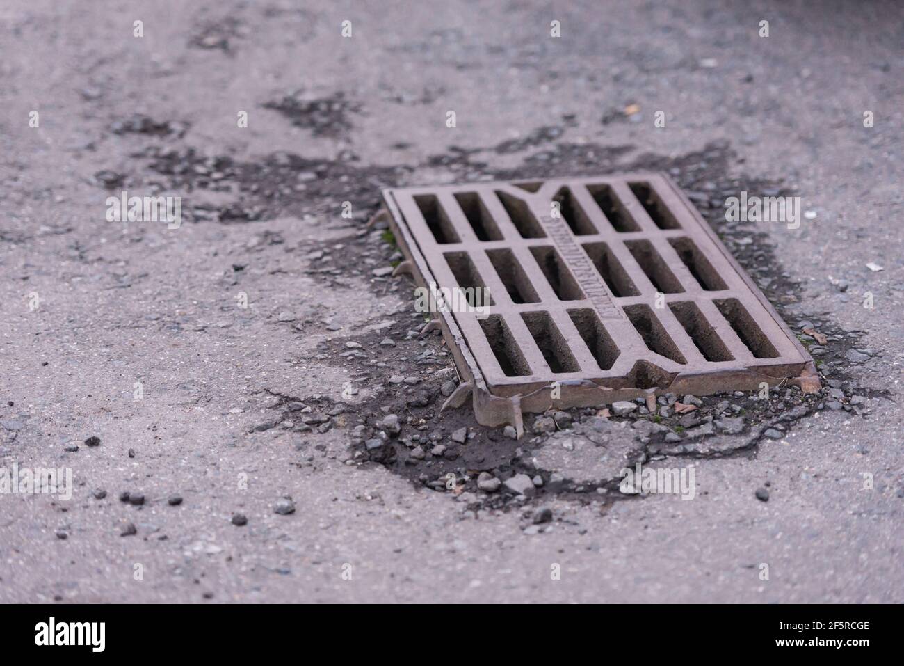 Rainwater grate in asphalt. An old rain grate protrudes from the asphalt. Stock Photo