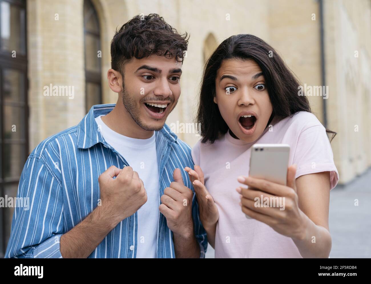 Emotional couple wins online lottery, celebration success. Excited friends using smartphone, shopping online Stock Photo