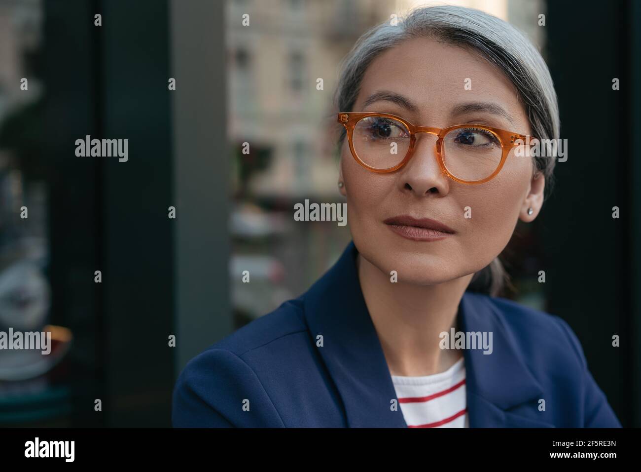 Close up portrait of pensive mature businesswoman looking away. Beautiful middle aged woman wearing eyeglasses standing outdoors. Vision concept Stock Photo