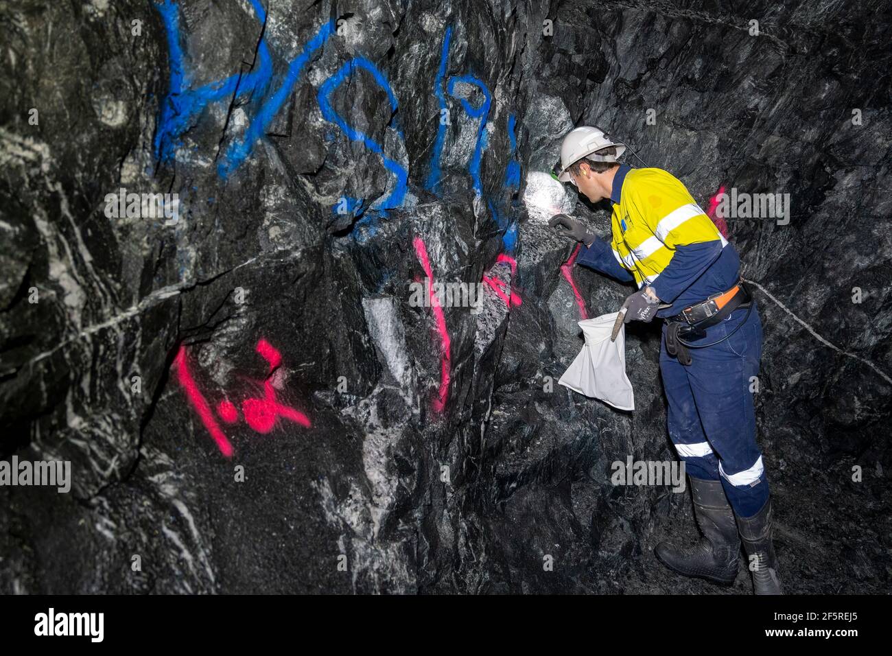 Geologist sampling ore and marking drilling instructions in underground mine shaft. Western Australia Stock Photo