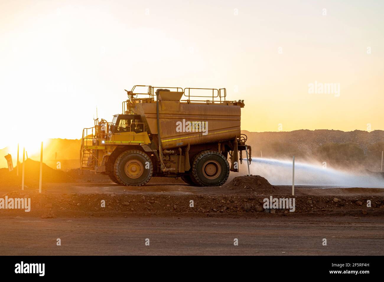 Water Cart dampening dusty mining roads at sunset in open pit mining area Stock Photo