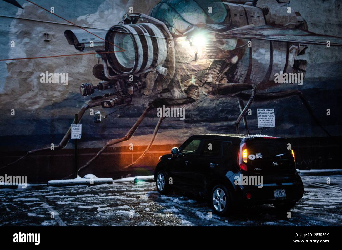 A small car parked with its lights on in front of a space station mural during a winter ice storm in the city of Richmond, Virginia the in the US. Stock Photo