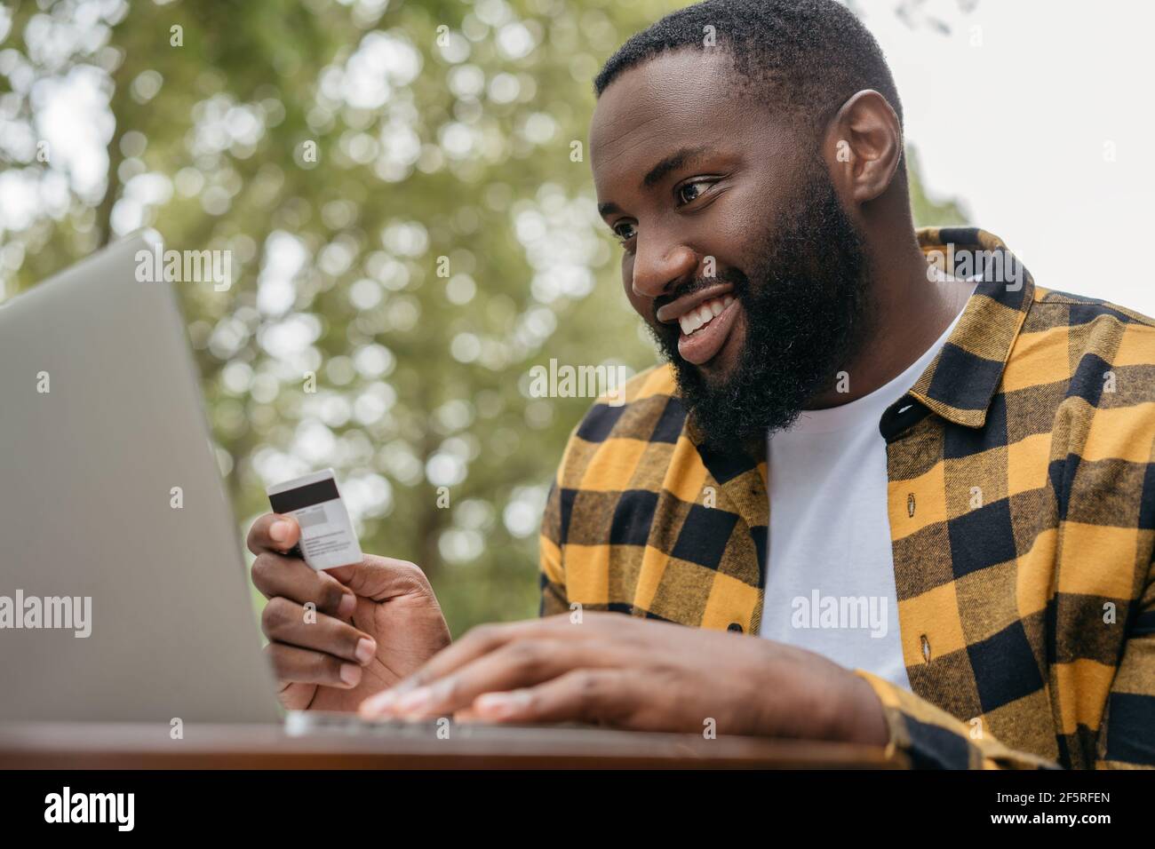 Young successful freelancer receive payment, check balance. Handsome African American man holding credit card, using laptop for online shopping Stock Photo