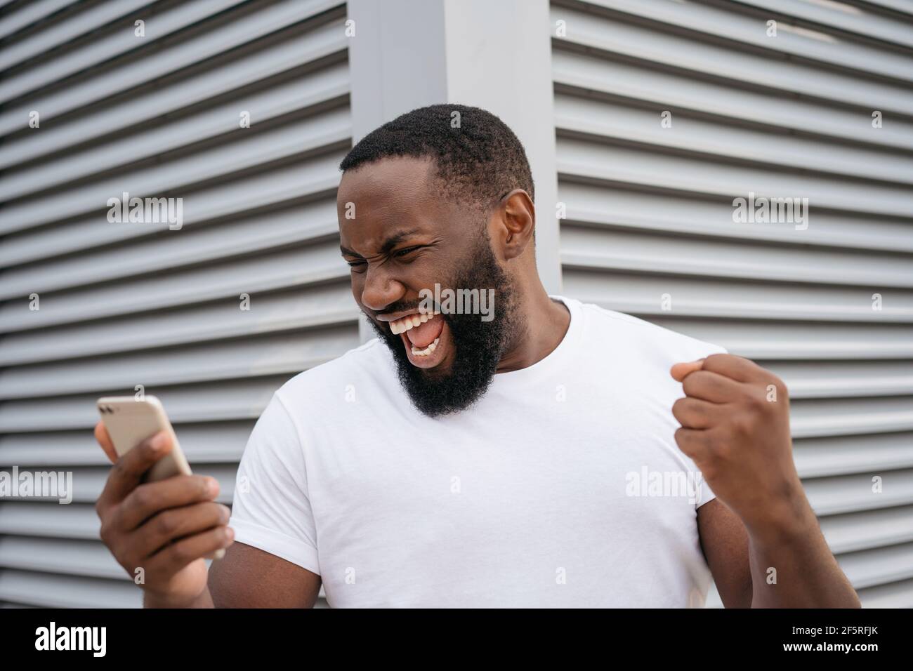 Portrait of overjoyed online lottery winner looking at digital screen, celebration success. Sport betting concept. Excited man using mobile phone Stock Photo