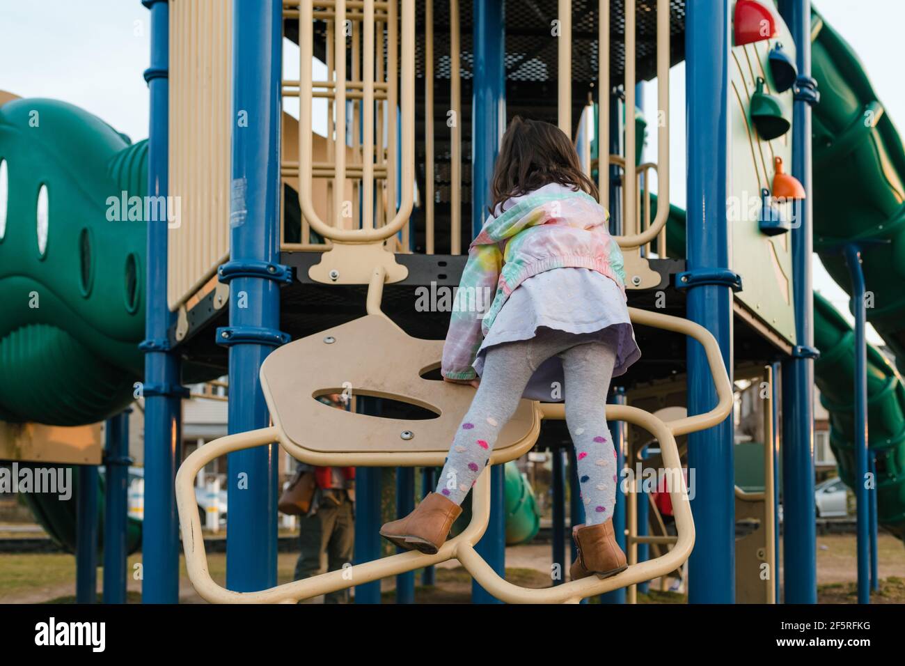 Girl climbing playground equipment wearing dress and tights Stock Photo