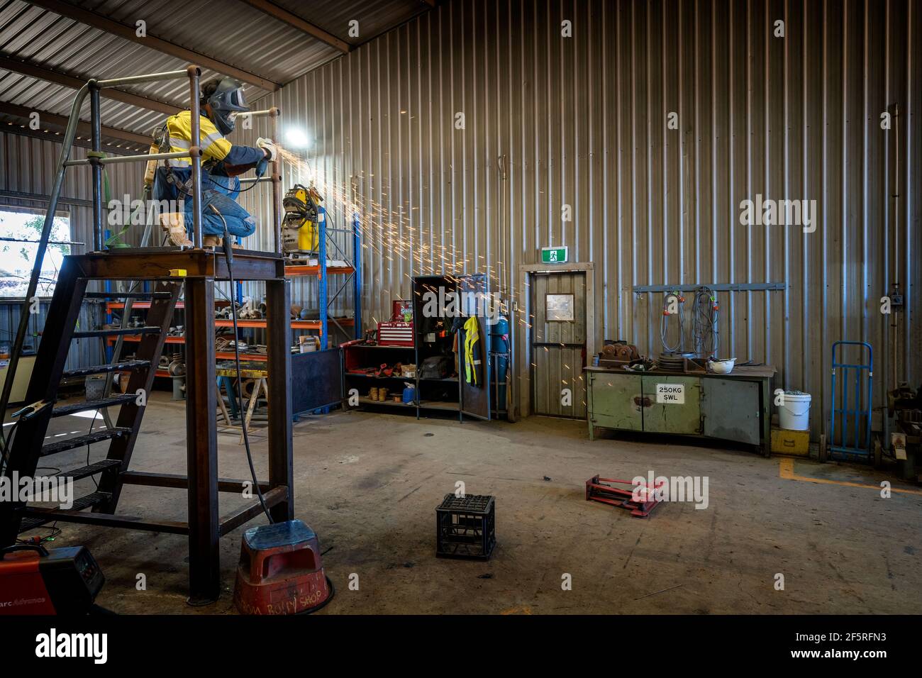 Boilermaker in protective clothing using grinder on metal stairway Stock Photo