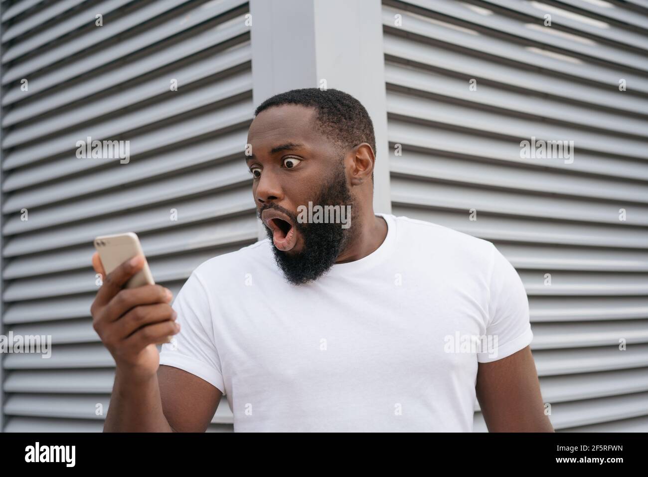 Shocked African American man with open mouth using mobile phone looking at digital screen. Amazed guy watching news online Stock Photo