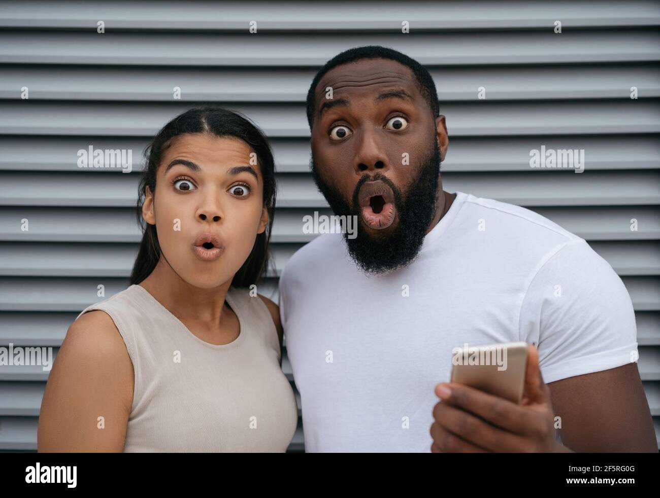 Excited African American man and woman holding mobile phone, shopping online looking at camera. Sport betting concept Stock Photo