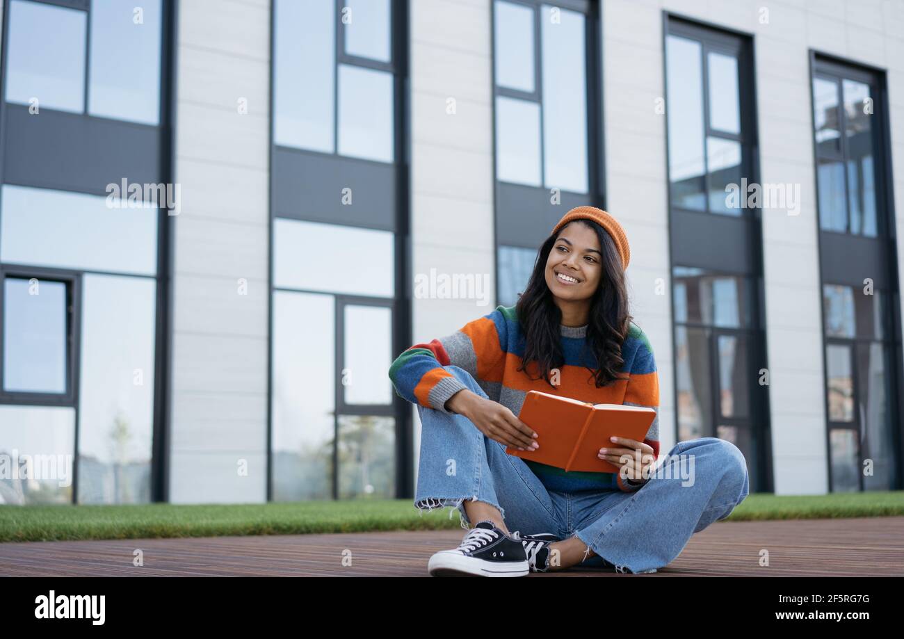 Beautiful African American woman reading book outdoors. Happy university student studying, learning language, exam preparation, education concept Stock Photo